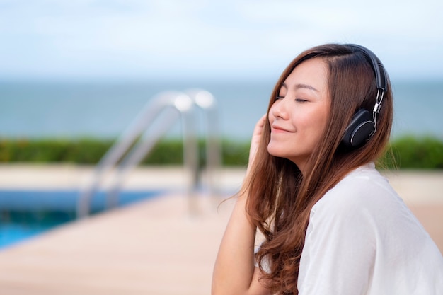 A beautiful asian woman listening to music with headphone while sitting by swimming pool