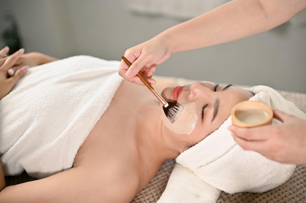 Beautiful Asian woman lying on massage table receiving facial treatment