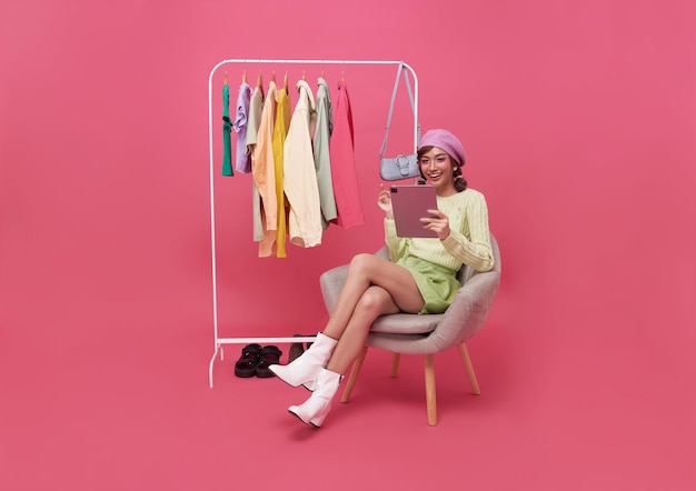 beautiful asian woman making online shopping and sitting on chair with new clothes on pink