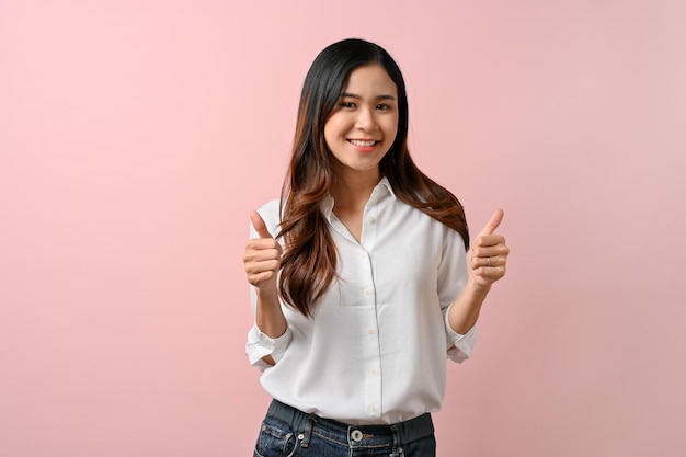 Beautiful Asian woman making a thumbs up gesture on pink isolated background