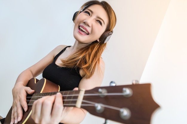 beautiful Asian Woman Playing Ukulele with happiness and joyful near widow white room