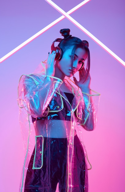 Beautiful asian woman in a raincoat listens music in headphones around colorful neon