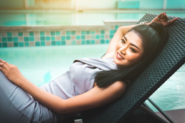 Photo beautiful asian woman relaxing on folder chiar and enjoy fresh air beside swimming pool ool