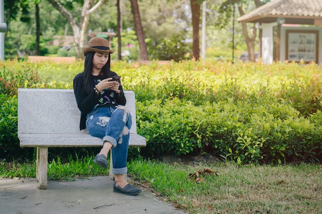 Beautiful asian woman sit on wood chair use phone in the park. 