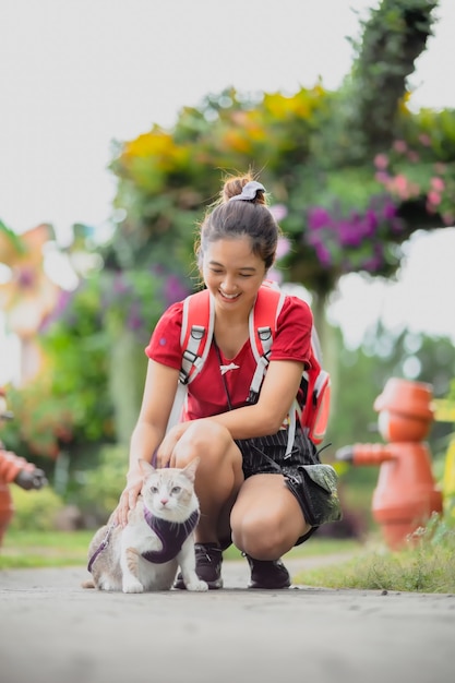 Beautiful Asian woman taking her cat for a walk. withflower garden background