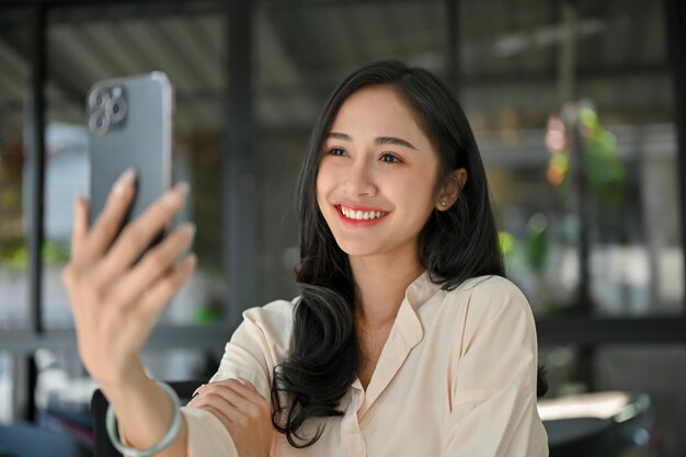 Beautiful Asian woman taking a selfie with her modern smartphone while relaxing at cafe