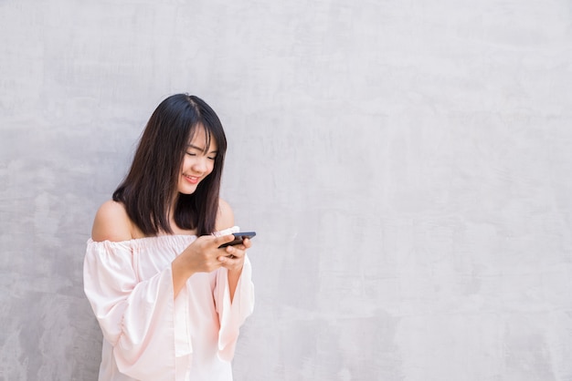 Beautiful asian woman using cellphone, over concrete wall