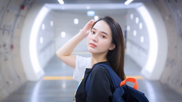 A beautiful Asian woman wearing a black shirt stood smiling as she entered a subway tunnel.