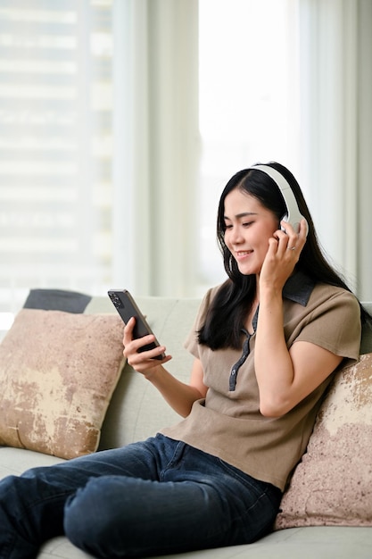 Beautiful Asian woman wearing headphones listening to music using her smartphone