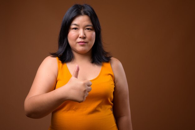 beautiful Asian woman wearing orange sleeveless dress on brown