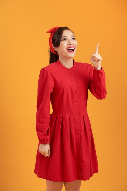 Beautiful Asian woman wearing a red dress and standing over an orange background