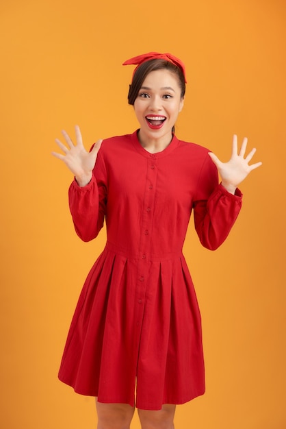 Beautiful Asian woman wearing a red dress and standing over an orange background