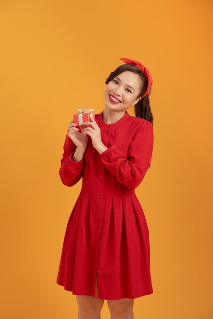 Beautiful Asian woman wearing a red dress and standing over an orange background