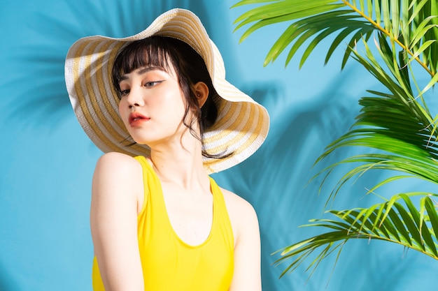 Beautiful Asian woman wearing yellow jumpsuit on blue with palm leaves