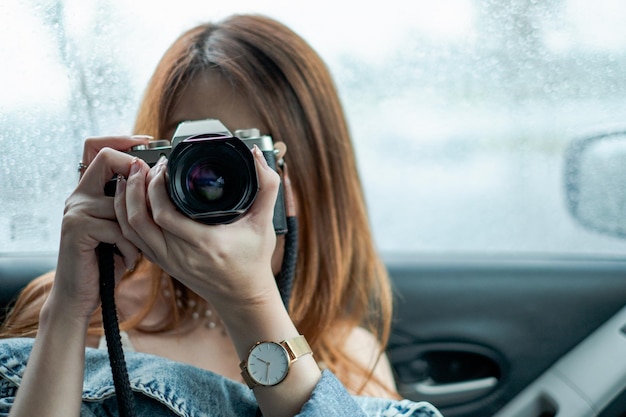 Beautiful asian woman with camera in car against rain drops background