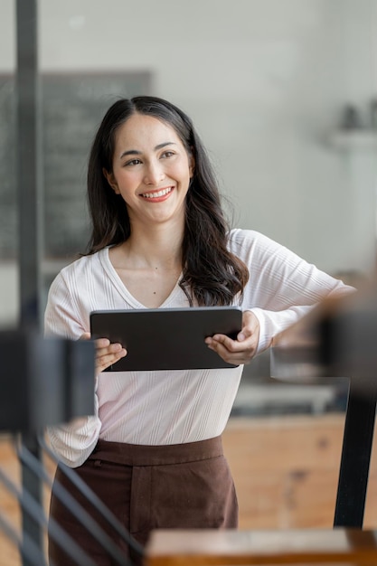 Beautiful asian woman with digital tablet sitting at cafe smiling and looking away outside