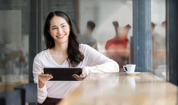 Beautiful asian woman with digital tablet sitting at cafe smiling and looking away outside