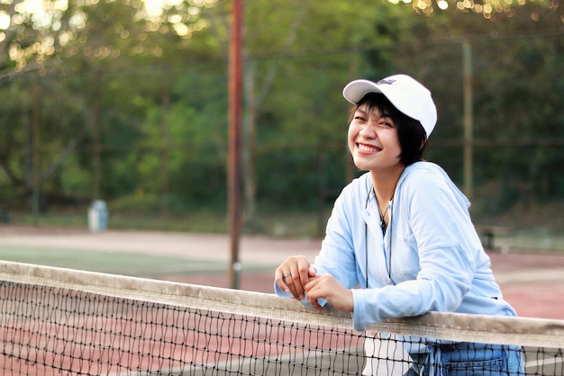 Beautiful Asian woman with short hair, wearing hat and smiling broadly on tennis court