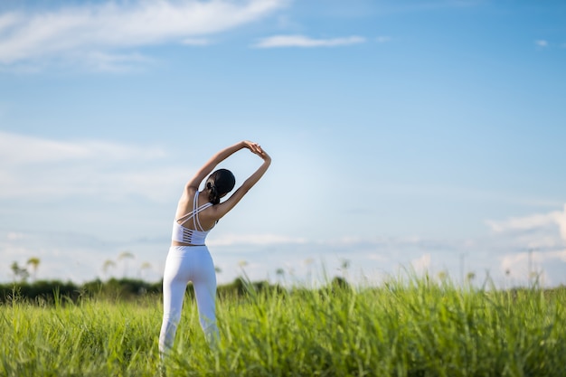 Beautiful Asian women in sportswear standing on Green grass with blue sky in the background ready to exercise outdoor. Healthy women concept. Running workout.