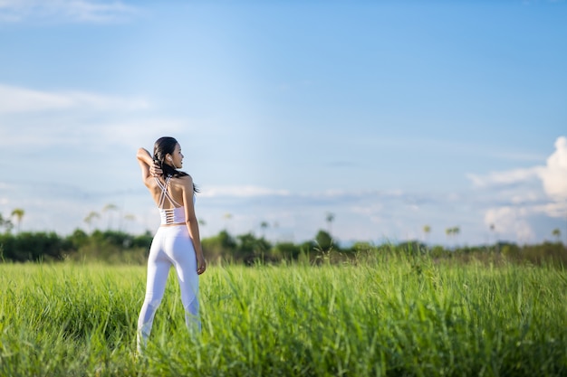 Beautiful Asian women in sportswear standing on Green grass with blue sky in the background ready to exercise outdoor. Healthy women concept. Running workout.