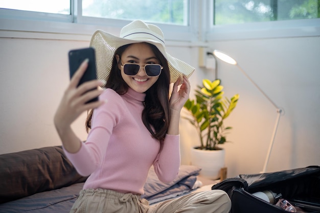 Beautiful Asian women using smartphone selfie and packing suitcases for travel