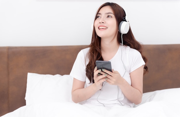 Beautiful Asian women wearing headphones listening to music streaming from their smartphones.