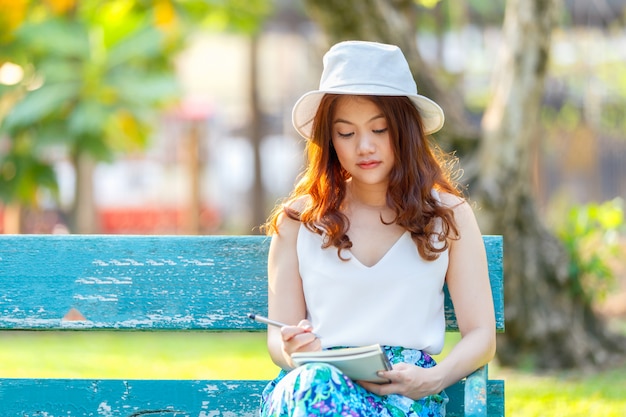 Beautiful asian women with pen writing notebook and sitting on a wooden bench and in a park