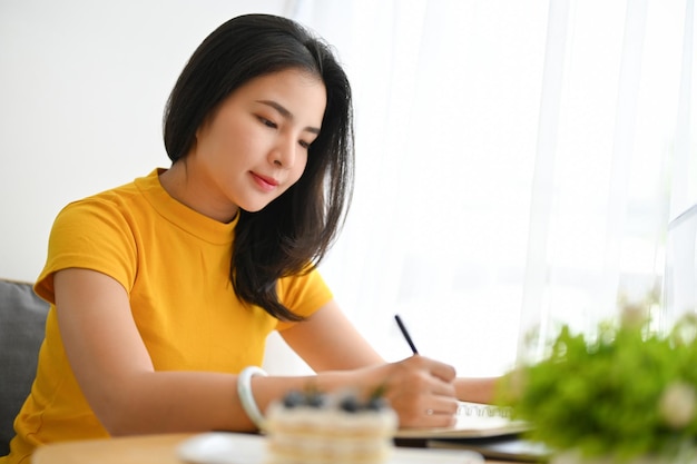 Beautiful Asian young female college student doing her homework on a school notebook