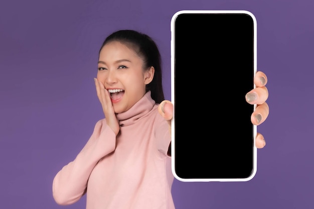 Beautiful Asian young woman Excited surprised girl showing big smart phone with blank screen white screen isolated on purple background Display Mock Up Image