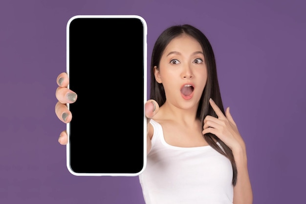 Beautiful Asian young woman Excited surprised girl showing big smart phone with blank screen white screen isolated on purple background Display Mock Up Image