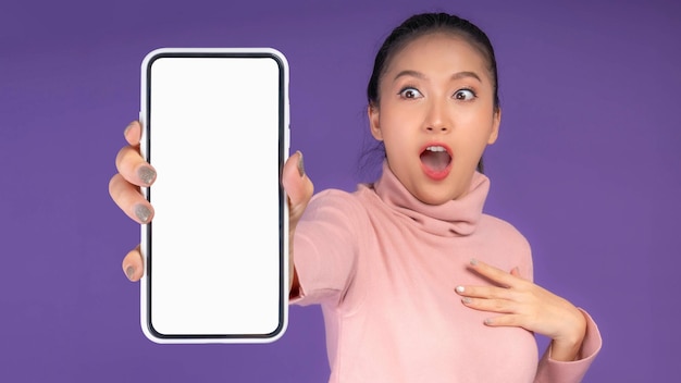 Beautiful Asian young woman Excited surprised girl showing smart phone with blank screen white screen isolated on purple background Mock Up Image