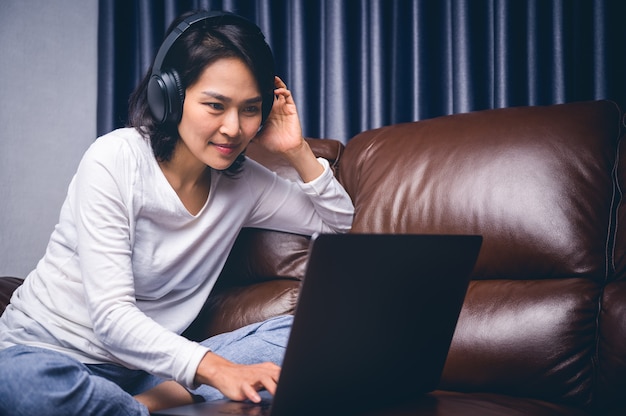 Beautiful asian young woman relaxing with her music playing with laptop on sofa.Work at home and happiness concept.