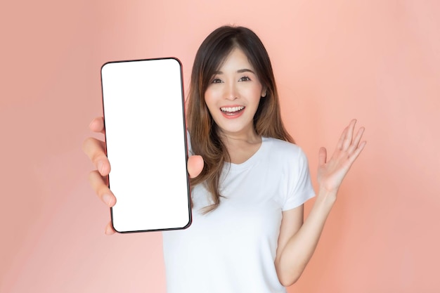 Beautiful Asian young woman showing big smart phone with blank screen white screen empty copy space for advertising banner isolated on pink background Mock Up Image