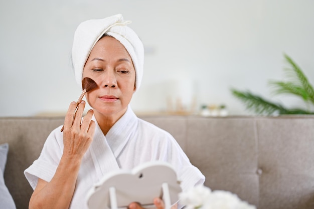 Beautiful Asianaged woman doing makeup applying brush on her cheek