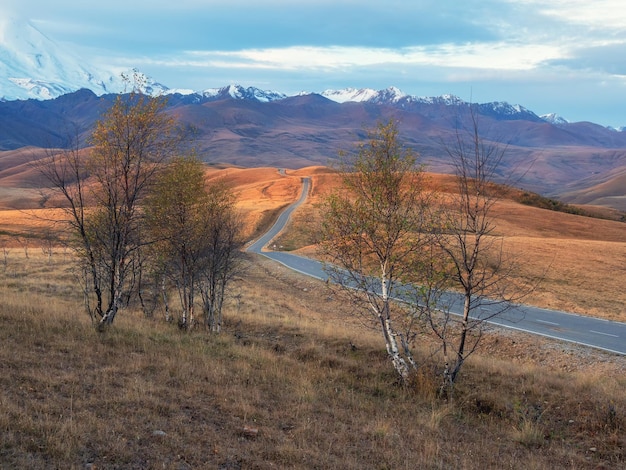 Beautiful asphalt freeway Early morning view of a road stretching into the distance through the picturesque autumn hills Winding road stretches into the distance to the snowcapped mountains