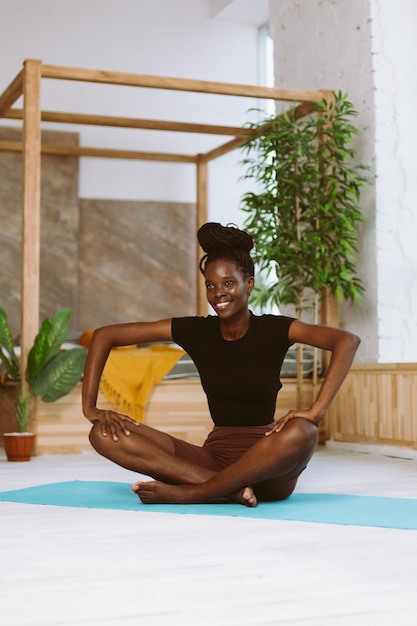 Beautiful and athletic afro american woman sitting in butterfly pose doing yoga on gymnastic mat in decorated studio Muscle stretching gymnastic exercises fitness keeping body fit