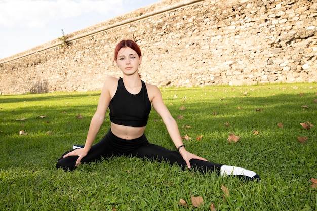 A beautiful athletic girl sits in a twine on the grass Sports and yoga in the park