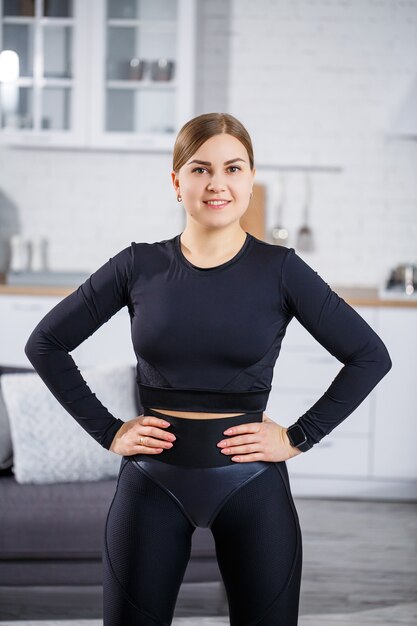 A beautiful athletic woman in a black top and leggings demonstrates a slender figure. Motivation to go in for sports. Healthy lifestyle.