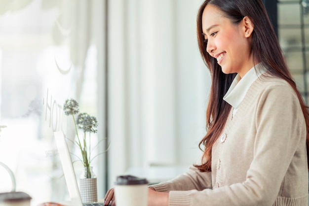 Beautiful attractive asian female freshness smile cheerful morning working with laptop coffee work from home with happiness enjoy garden view asian young woman with window light garden background