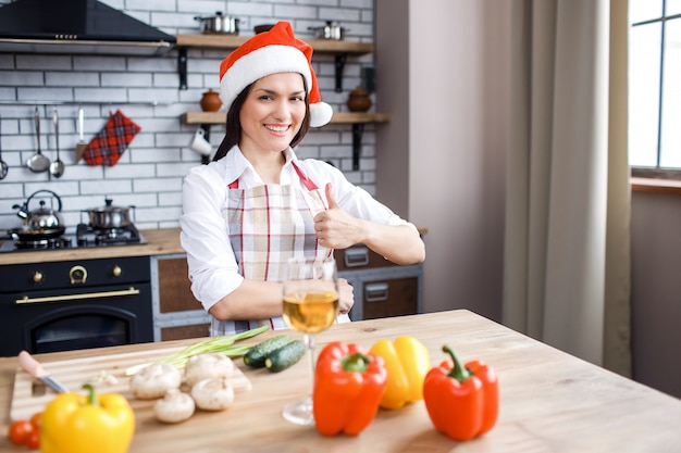 Beautiful attractive woman in red hat stand in kitchen and pose on camera