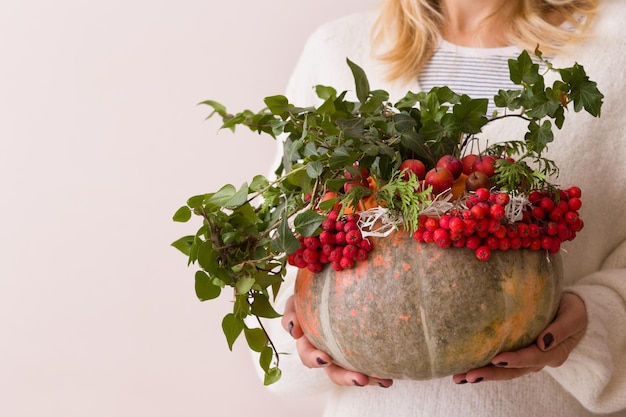 Beautiful autumn composition in a pumpkin vase in woman's hands Flower and red berries arrangement