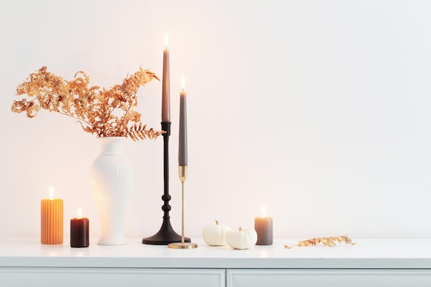 Beautiful autumn home decor with burning candles in white interior