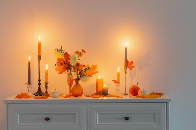 Beautiful autumn home decor with burning candles in white interior