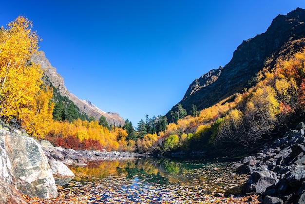 Beautiful autumn landscape with clear green water of a mountain lake and trees with autumn foliage reflected in it