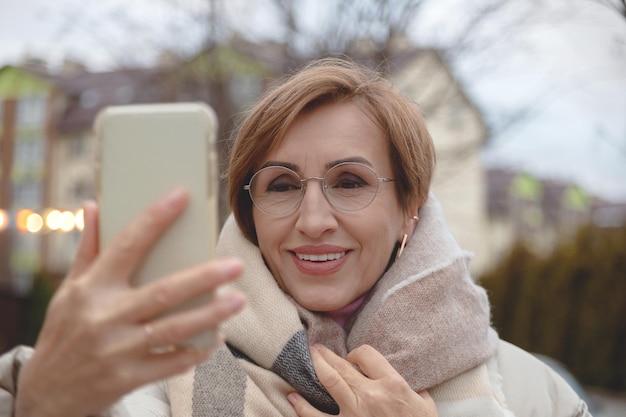 Beautiful baby boomer woman of middle age takes selfie on smartphone on the street