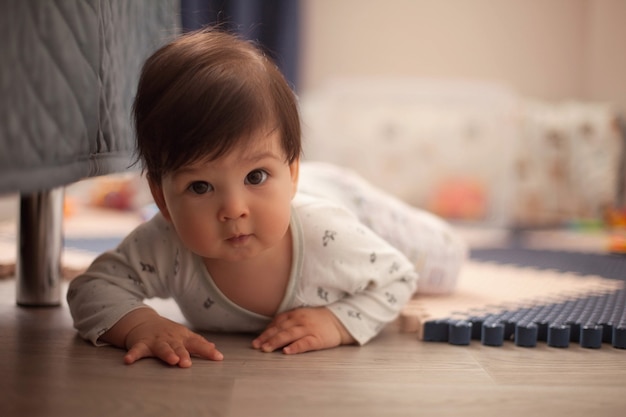 Beautiful baby boy with dark hair in the bright pajamas learning to crawl and lie on his stomach on the floor in the nursery