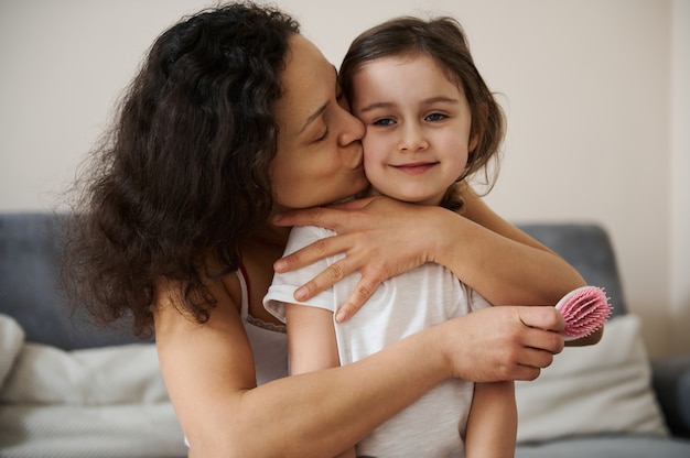 Beautiful baby girl feels happy when her loving mother hugging and kissing her tenderly. Concept of carefree childhood and happy motherhood. Love, tenderness , affection concept