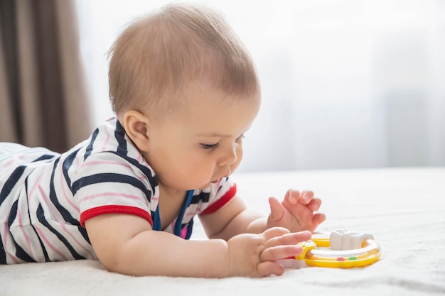 beautiful baby lies on the bed and plays by yellow toy