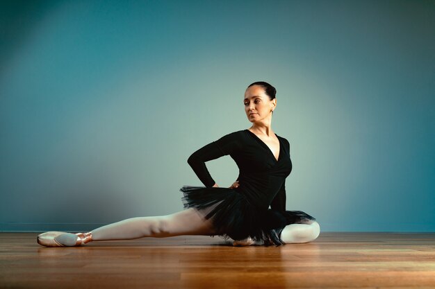 Beautiful ballerina in pointe shoes sitting on the floor