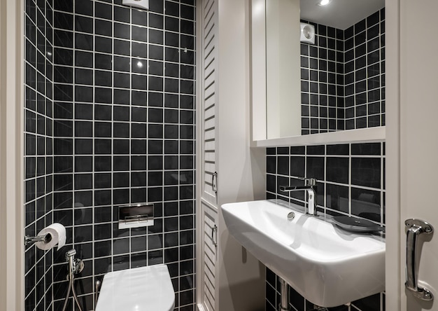 Beautiful bathroom with black glossy square tiles white ceramic sink with faucet and wooden lockers